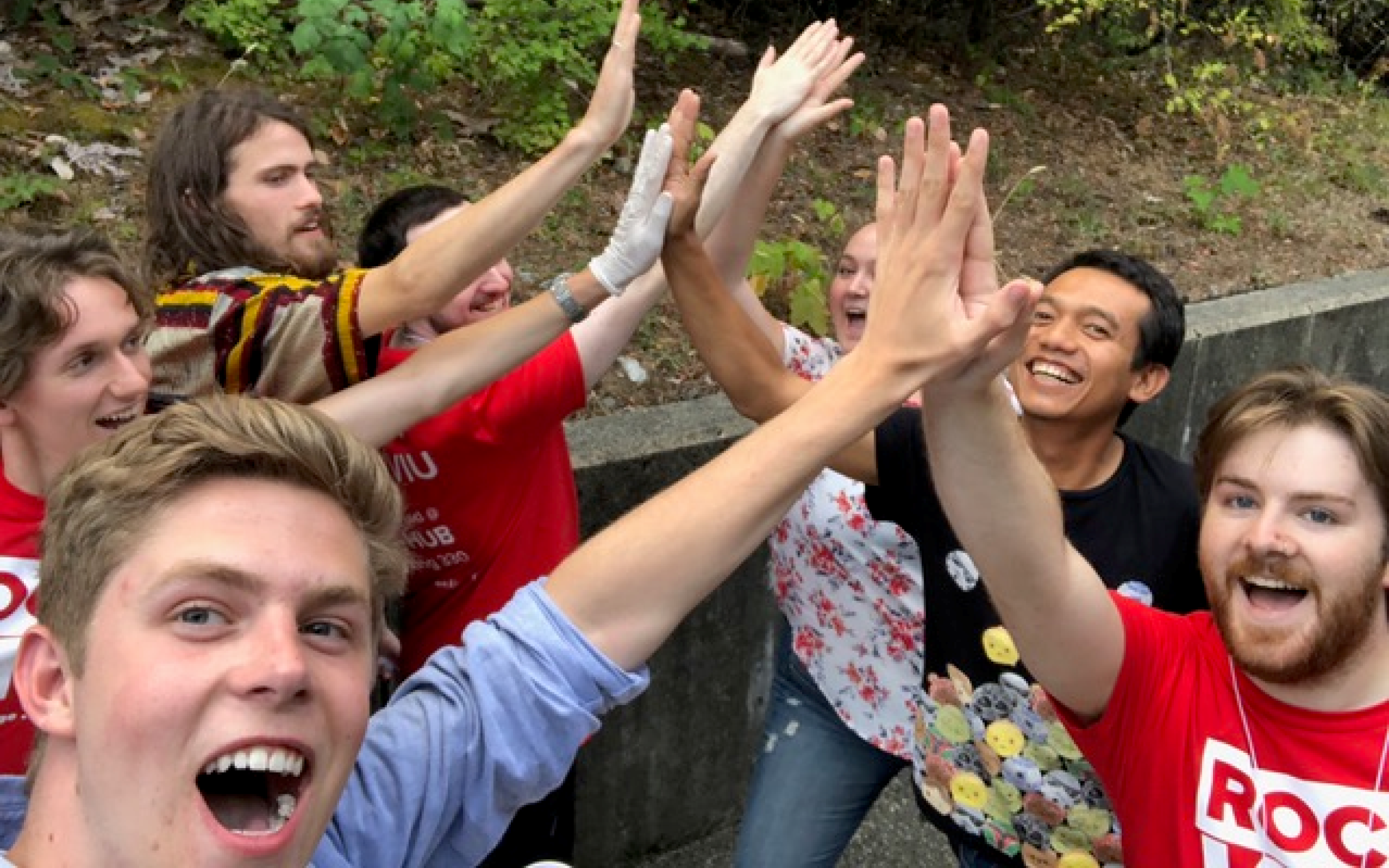 A group of students outside hi-fiving each other with big smiles 