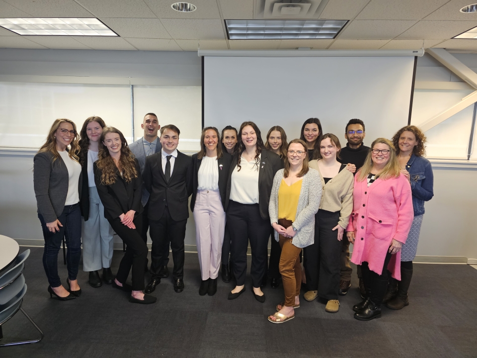 a group of fifteen students and faculty professionally dressed nd smiling standing in a line