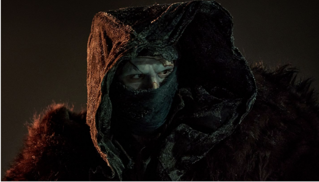 Frankenstein's Creature, wearing a hood and a mask, staring intensely to his left. 