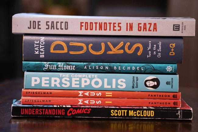Six graphic novels stacked in a pile, with only their colourful spines showing.