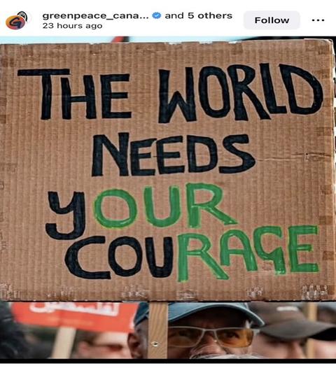 Man wearing a hat and sunglasses holding up a cardboard protest sign.
