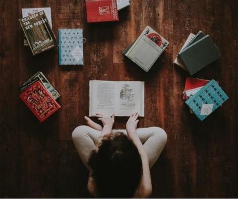 From overhead, a girl sits crosslegged surrounded by books